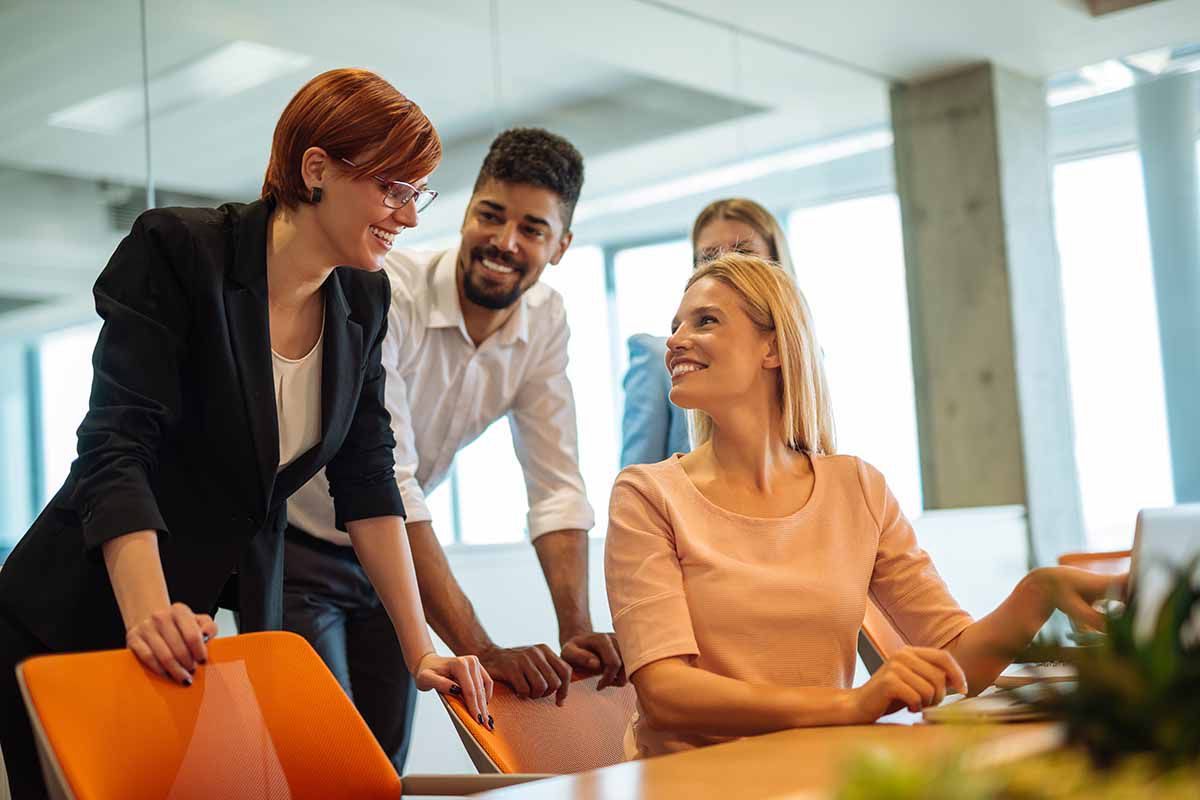 A group of colleagues smiling chatting together looking at a laptop.