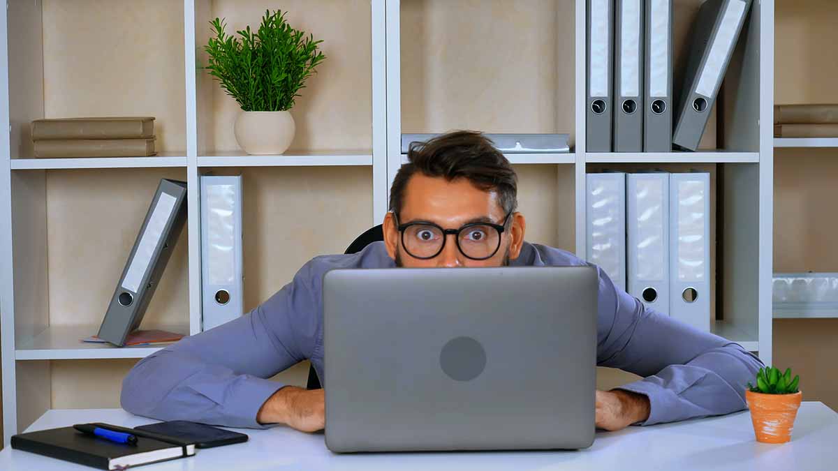 A young worker looking surprised looking at his laptop in an office setting.